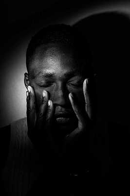 portrait of a young black man with his hands on his face.